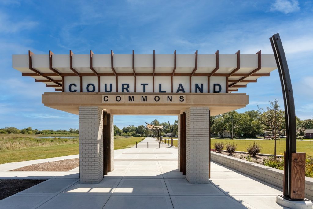 Entrance structure at Courtland Commons in Mundelein, Illinois, featuring a modern walkway and surrounding green space on a sunny day.