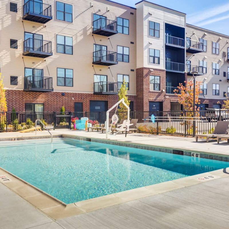 Outdoor swimming pool with bright blue water and concrete deck surrounded by Station 250 apartment buildings with private balconies in Mundelein IL